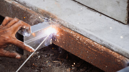 Extreme danger close-up of a worker's bare hand holding a metal tube during arc welding with bright...