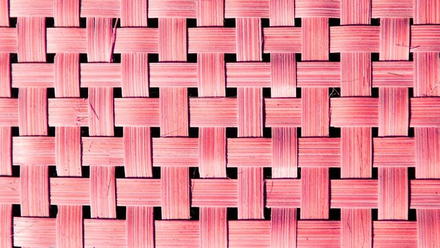 Close-up of a woven texture in shades of pink. The image showcases a repeating pattern of interlaced strips, creating a grid-like or basket-weave effect