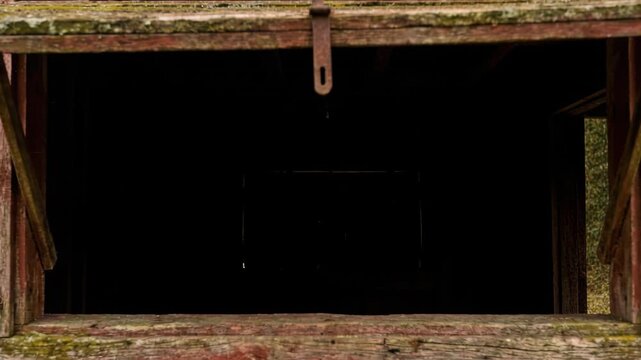 Close-up of a weathered rustic barn window with peeling red paint and moss. A metal latch secures the aged wooden frame around a dark opening