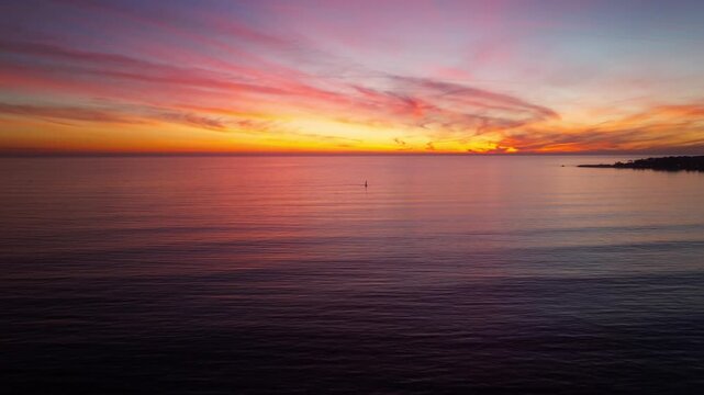 A beautiful and colorful ocean sunset as seen from Santa Cruz California looking over the pacific ocean towards a lone sailboat in a serene panning aerial drone shot