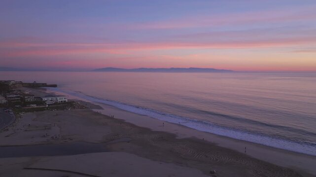 A beautiful and colorful ocean sunset seen from Santa Cruz California state beach looking over the pacific ocean towards Monterey California in a serene panning aerial drone shot with waves crashing