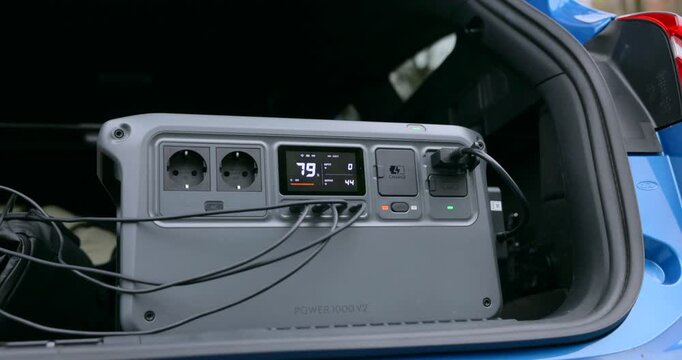 A portable power station is shown inside the trunk of a car providing backup power and electricity for camping outdoor activities travel and emergencies.
