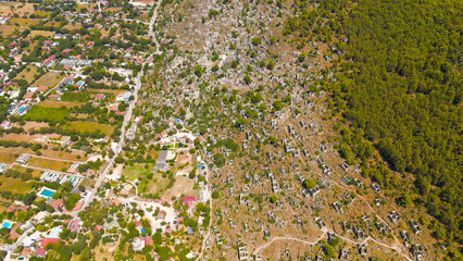 Kayakoy, Turkey. Aerial drone view of the abandoned ghost town ruins and stone houses on mountain slopes under clear blue sky and bright sunlight.. Aerial View