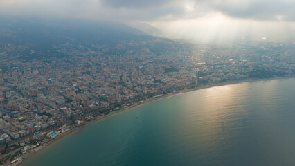 Alanya, Turkey. Aerial shot of Alanya Lighthouse overlooking Antalya Bay and city beaches with dramatic sunbeams through clouds in summer morning.. Aerial View