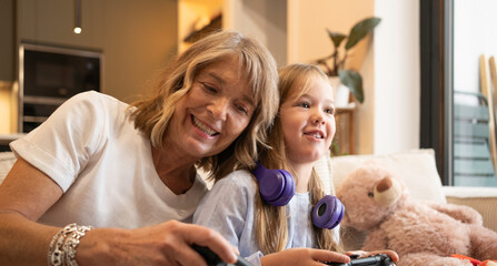 Portrait of happy grandmother and granddaughter playing together with video game controllers on a couch