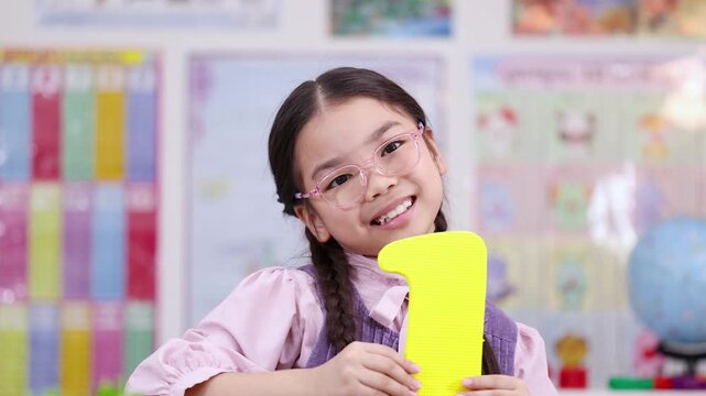 Happy schoolgirl holding number one in colorful classroom