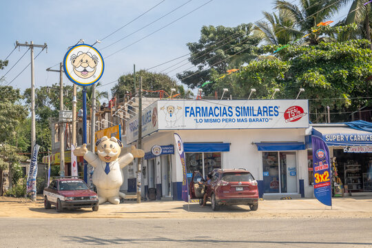 Huatulco, Oaxaca, Mexico. Dec 15, 2025. A Farmacias Similares pharmacy with the brand's name, logo, and a large inflatable Dr. Simi mascot standing on a sunny street in Mexico.