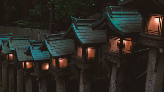 : A row of traditional Japanese stone lanterns with glowing warm lights and teal roofs - Powered by Adobe