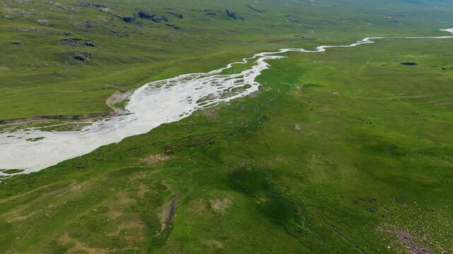 Aerial View Of A Melting Glacier River Through Green Meadows Through Valleys In Kyrgyzstan.