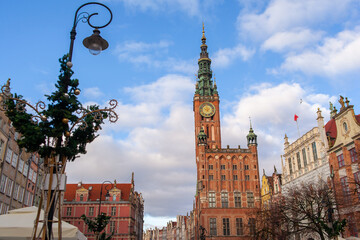 Naklejka premium A clock tower stands tall in city sqare. Street in an Old town and Town Hall in Gdansk, Poland. Panoramic view. Historical city of Gdansk (Danzig), Poland, Europe.