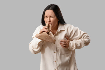 Young woman with paper bag having heart attack on light background