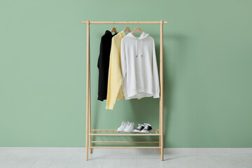 Rack with stylish hoodies near green wall