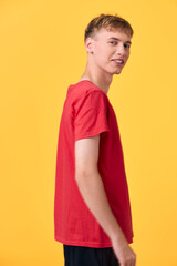 Young man in a red shirt turns slightly to the side against a bright yellow background, presenting...