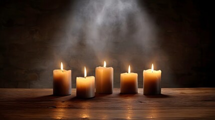 Five lit candles cast a warm glow on a rustic wooden table illuminated by a dramatic spotlight creating atmospheric mist