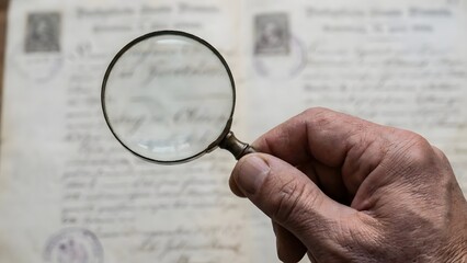 Hand holding magnifying glass over document.