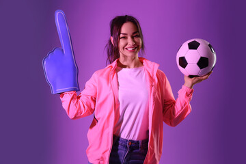 Female soccer fan with ball and foam hand on purple background