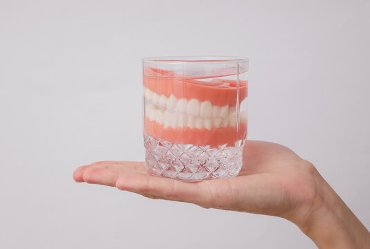 Hand holding dentures in glass on white background
