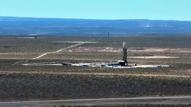 A fracking rig is seen in the distance. The Vaca Muerta plateau. 4K drone footage.