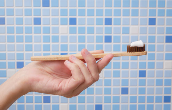 Hand holding eco friendly wooden toothbrush with toothpaste on bathroom tile background
