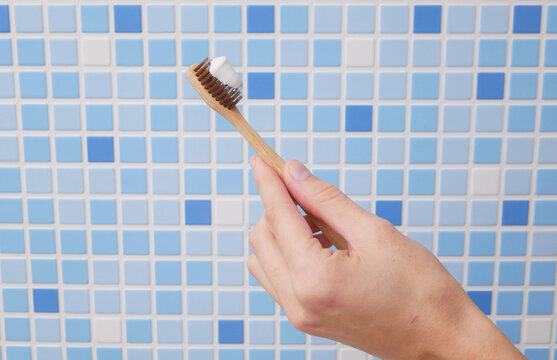 Hand holding eco friendly wooden toothbrush with toothpaste on bathroom tile background