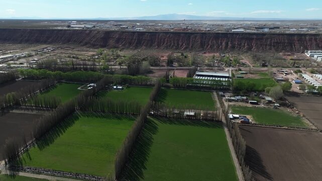 A drone flies over the low-lying green farmlands of A&ntilde;elo. In the background, the plateau with its oil extraction activity is visible. Far in the distance, the Auca Mahuida volcano can be seen.