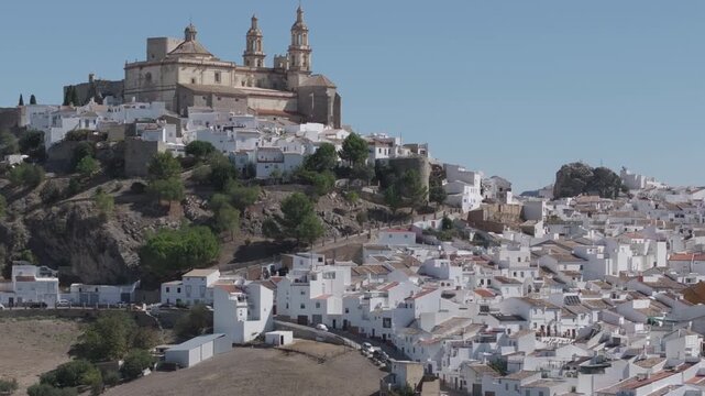 Cinematic aerial drone establishing reveal shot, panorama wide view of the white town village of Olvera in Andalusia, Spain, Europe. Traditional Spanish castle and church on hill, with olive trees