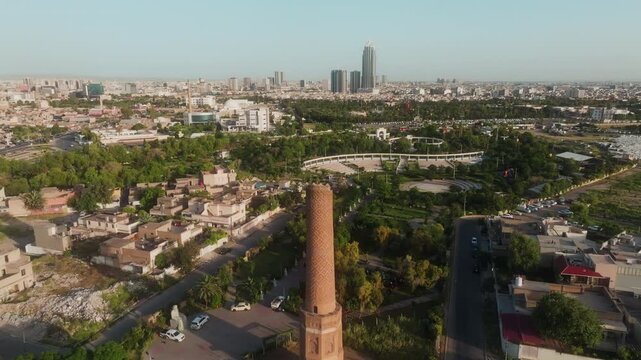 Drone advancing over Mudhafaria Minaret toward Erbil skyline and park sports field.