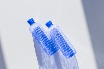 Blue plastic water bottles on white blue background with sunlight shadow and sun flare, Minimal top...