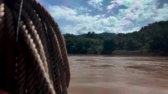 Coiled rope on a slow boat along the Mekong River, Laos, with green banks and sky.