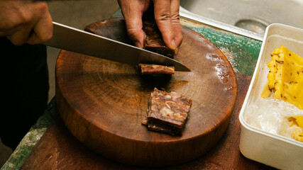 Hands cutting cooked pork on wooden chopping board
