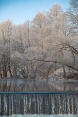 Trees in the snow near a river and a waterfall, winter