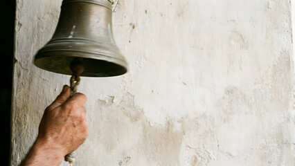 Hand holding a bronze bell against a wall.