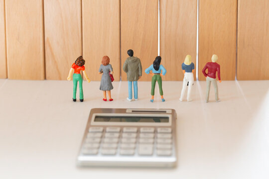 立ちはだかる積み木の壁を前に並んで立つ男女のフィギュアと計算機 年収の壁 お金のイメージ 