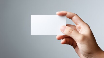 Obraz premium Hand holding a blank white card, ready for branding or message, against a neutral background