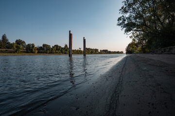 Weathered pilings stand in the calm waters of the Sacramento River during a hazy summer sunset