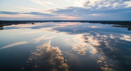 Calm lake reflecting sunset clouds and trees with distant shoreline