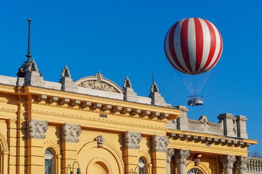 A hot air balloon as a viewing platform for tourists is flying high in the sky above the treetops and above the Secheni baths palace in Budapest, Hungary