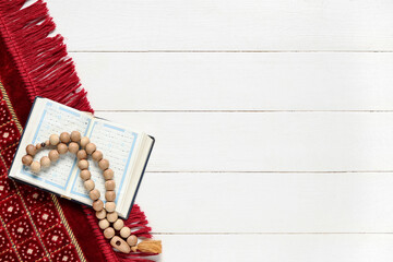 Koran with tasbih and prayer carpet on white wooden background. Ramadan celebration
