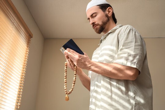 Young Muslim man with Koran and tasbih praying at home. Ramadan celebration