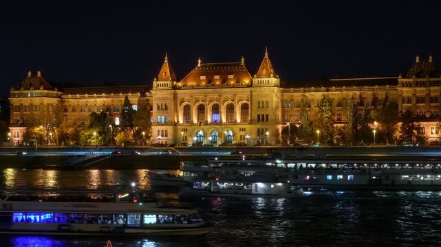 architecture with warm golden illumination reflecting in the river water at night, featuring passing cruise boats in Budapest city