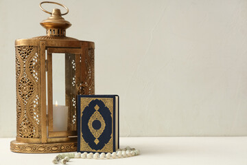 Lantern with burning candle, Koran and prayer beads on white grunge background