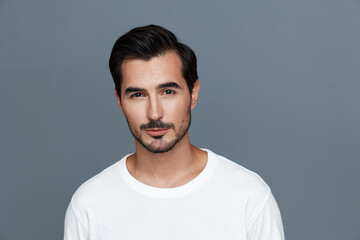 Fototapeta premium Stylish man with short dark hair wearing a white t-shirt looks confidently at the camera against a gray background, exuding charisma and charm.