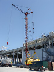 Construction site with large crane lifting materials next to a building and vehicles