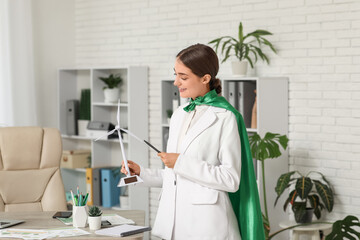 Female engineer in superhero cape with wind turbine model at office