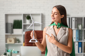 Female engineer in superhero cape with wind turbine model at office
