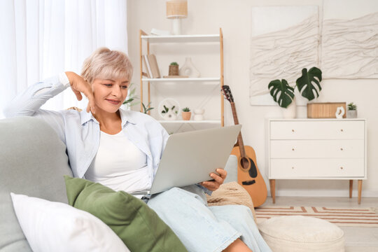 Mature woman using laptop on sofa at home - Powered by Adobe