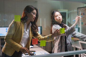 Businesswomen planning strategy on glass board, brainstorming ideas
