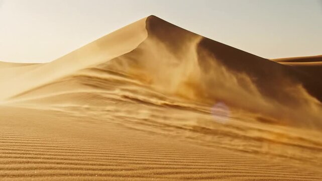 Wind whips sand across a vast desert dune, forming dynamic patterns on its golden surface