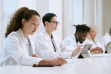 Multiethnic group of young adult and middle aged men and women working at table, Asian woman writing on paper, Black man using digital tablet, focused on scientific research