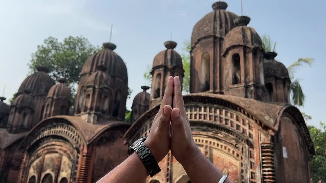 Hands of a man, praying in front of a old terracotta temple in Bengal, India.